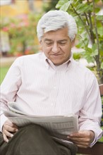 Senior Hispanic man reading newspaper