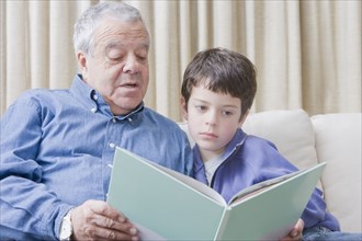Hispanic grandfather reading book to grandson