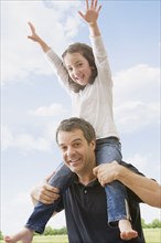 Hispanic father carrying daughter on shoulders