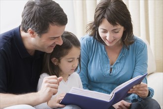 Hispanic parents reading book to daughter