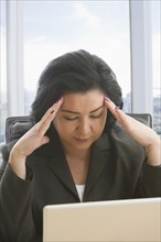 Hispanic businesswoman with headache using laptop