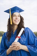 Mixed race woman wearing graduation cap and gown holding diploma