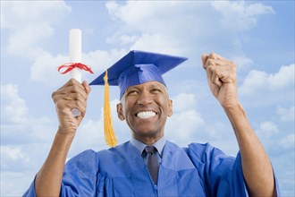 Mixed race man in graduation cap and gown holding diploma