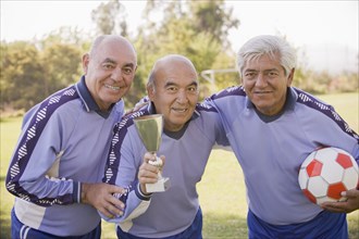 Senior Chilean soccer players holding trophy and soccer ball