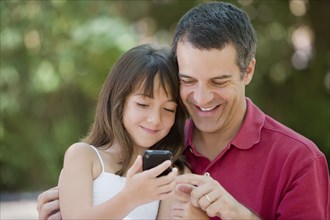 Hispanic father and daughter text messaging on cell phone