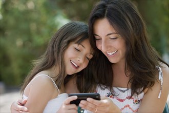 Hispanic mother and daughter text messaging on cell phone