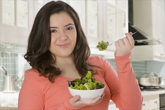 Hispanic teenage girl eating salad in kitchen