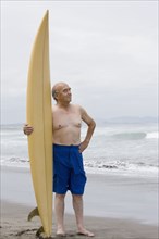 Senior Hispanic man holding surfboard on beach