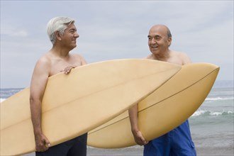 Senior Hispanic men holding surfboards on beach