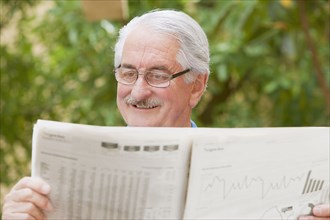 Senior Hispanic man reading financial newspaper