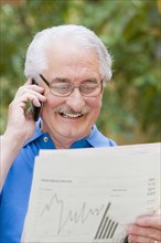 Senior Hispanic man reading financial newspaper and talking on cell phone