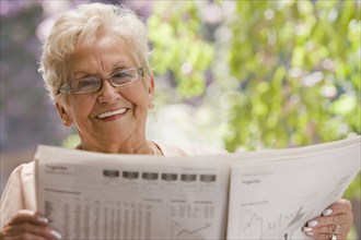 Senior Hispanic woman reading financial newspaper
