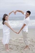 Hispanic couple making heart shape with arms on beach