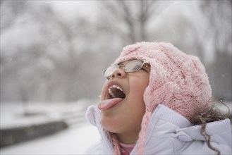 Hispanic girl catching snowflakes on tongue
