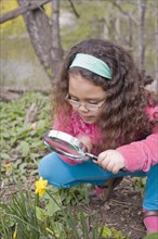 Hispanic girl looking at flower with magnifying glass