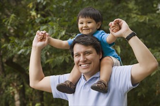Hispanic father carrying son on shoulders