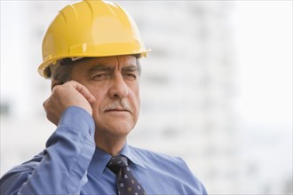 Hispanic businessman wearing hard hat and talking on cell phone