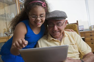 Older Hispanic man using digital tablet with granddaughter