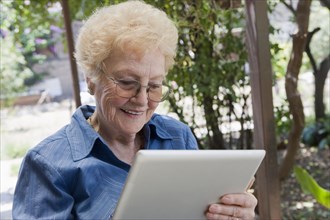 Older Hispanic woman using tablet computer outdoors