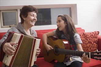 Older Hispanic woman playing music with granddaughter