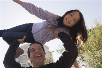 Hispanic man lifting daughter over his head