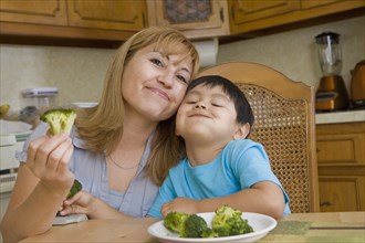 Hispanic mother and son eating broccoli