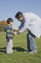 Hispanic father zipping son's sweater in field
