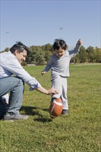 Hispanic father and son playing football outdoors