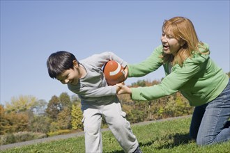 Hispanic mother and son playing football outdoors