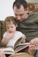Hispanic father reading to daughter on sofa
