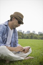Hispanic man using cell phone in grass at park
