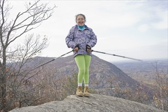 Portrait of smiling Hispanic girl on rock with hiking poles