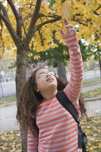 Hispanic girl reaching for autumn leaves overhead
