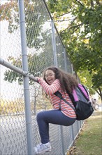 Portrait of enthusiastic Hispanic school girl climbing fence