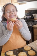 Portrait of smiling Hispanic girl eating muffin in kitchen