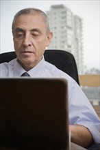 Close up of Hispanic man using laptop in urban office