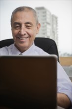 Close up of smiling Hispanic businessman using laptop