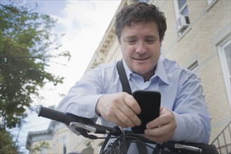 Hispanic businessman using cell phone on bicycle on city street