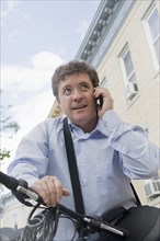 Hispanic businessman talking on cell phone on bicycle on city street