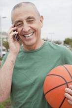 Hispanic senior man with basketball talking on cell phone
