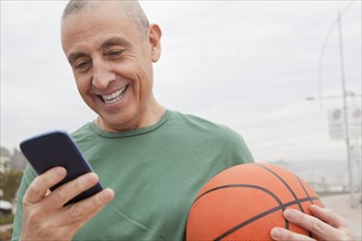 Hispanic senior man with basketball using cell phone