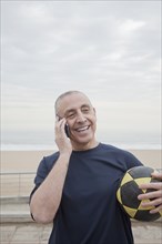Hispanic senior man with soccer ball talking on cell phone