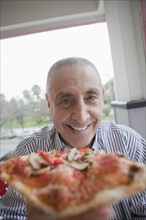 Hispanic senior man sharing slice of pizza