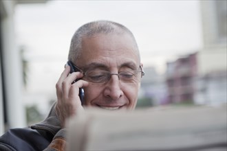 Hispanic senior man talking on cell phone and reading newspaper