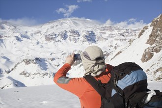 Hispanic hiker taking photograph of snowy mountain range