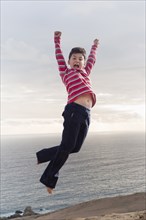 Hispanic boy jumping for joy on beach