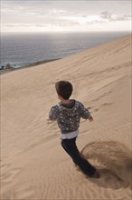 Hispanic boy running on sand dune on beach