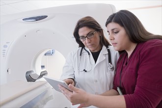 Hispanic doctor and nurse using digital tablet in MRI room