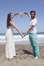 Hispanic couple forming heart-shape with arms at beach