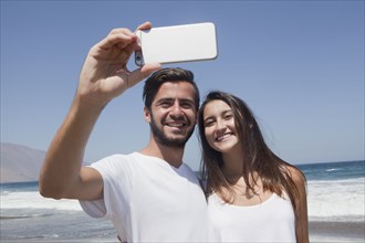Hispanic couple posing for cell phone selfie at beach